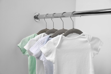 Baby bodysuits hanging on rack near white wall, closeup