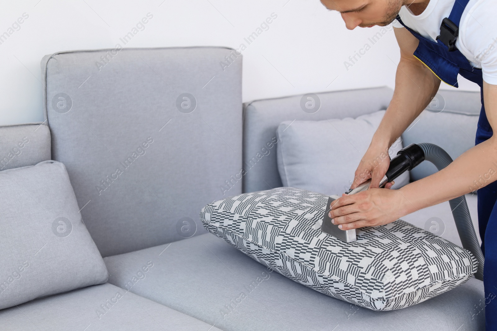 Photo of Male worker removing dirt from sofa with professional vacuum cleaner indoors