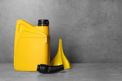 Photo of Yellow canister with motor oil and plastic funnel on light grey table. Space for text