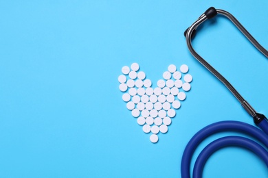 Heart shape made of pills near stethoscope on light blue background, flat lay. Space for text