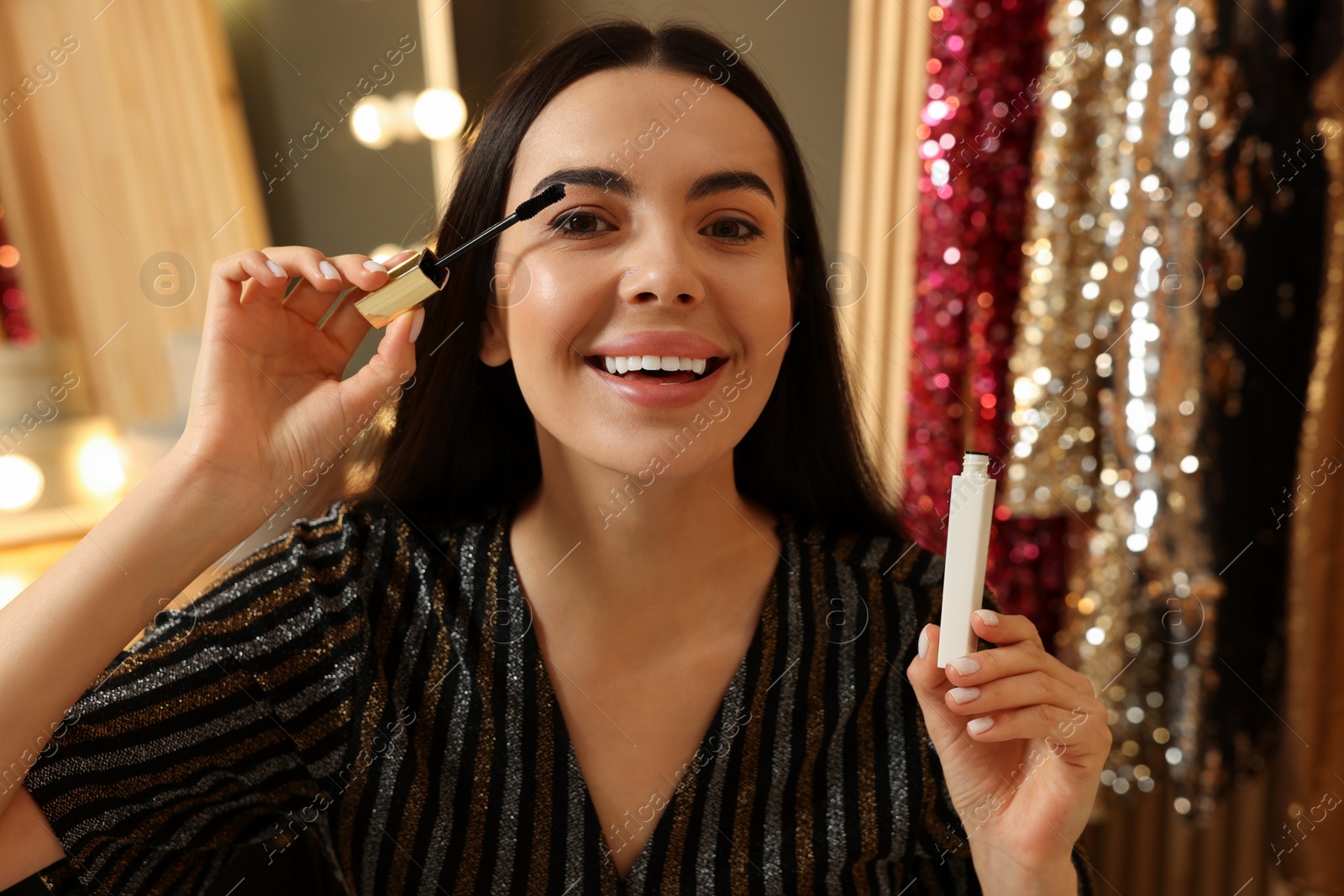 Photo of Beautiful young woman applying mascara in dressing room