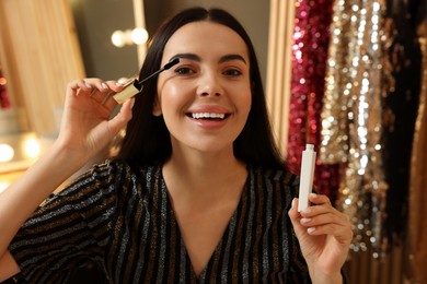 Beautiful young woman applying mascara in dressing room