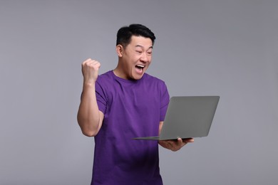 Emotional man with laptop on grey background
