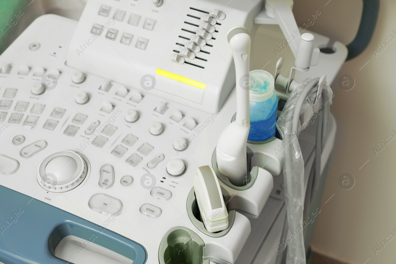 Photo of Ultrasound control panel with ultrasonic transducers and transmission gel near white wall, closeup