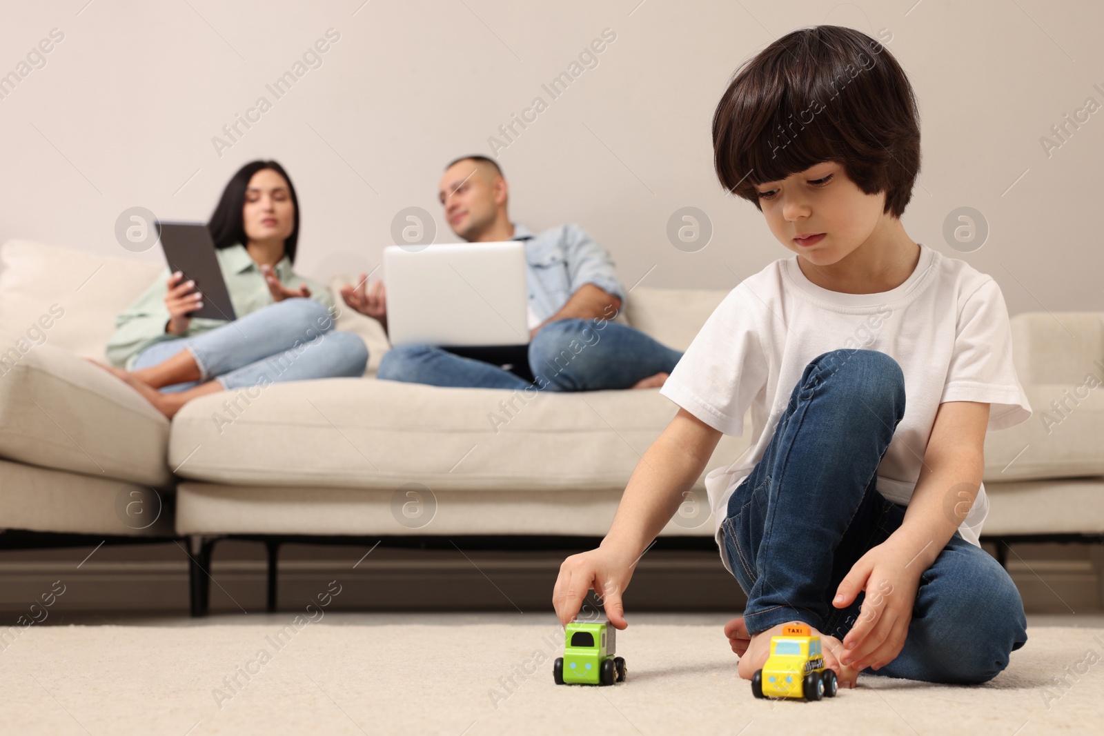 Photo of Child playing with toys and parents working on sofa at home