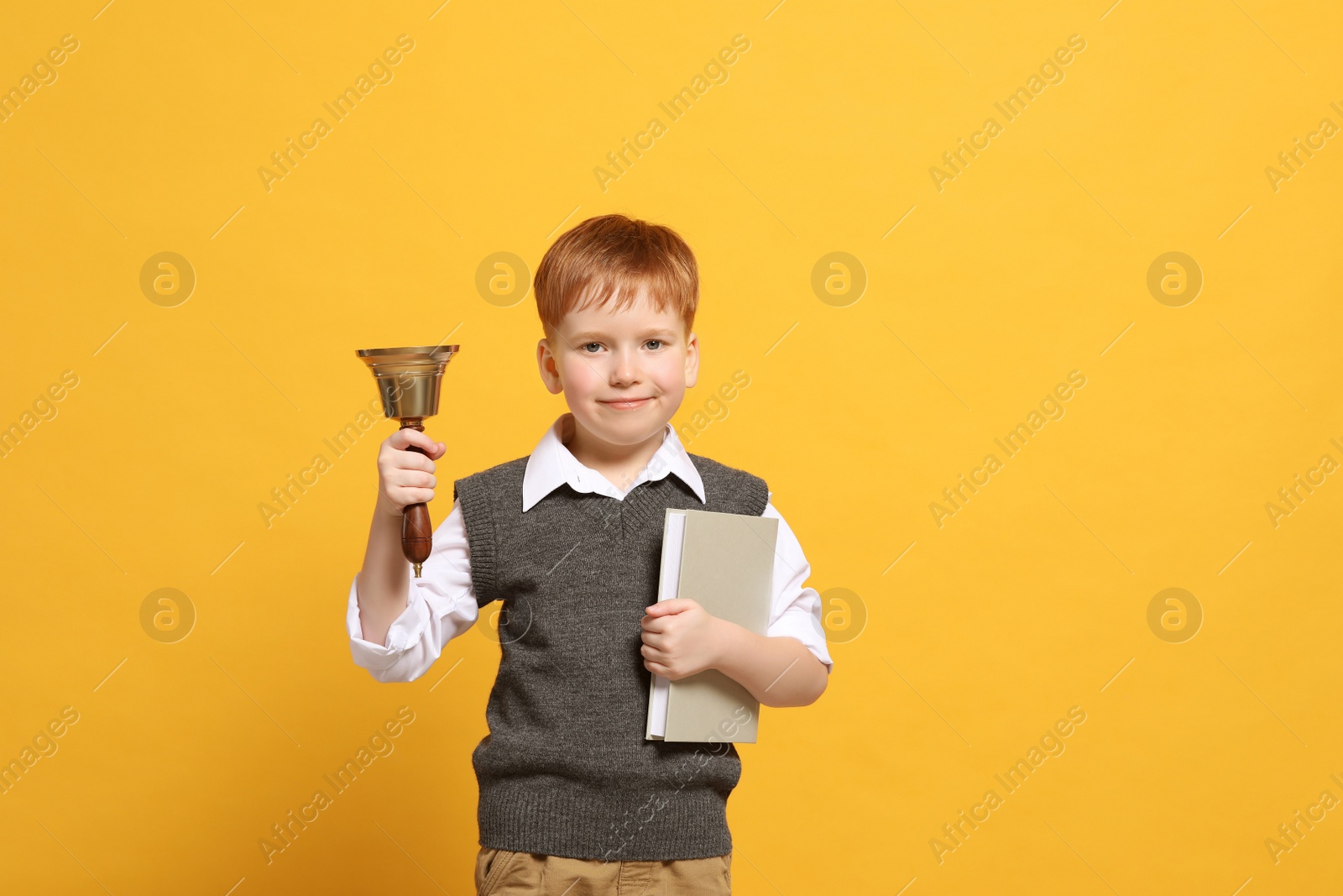 Photo of Pupil with school bell and book on orange background