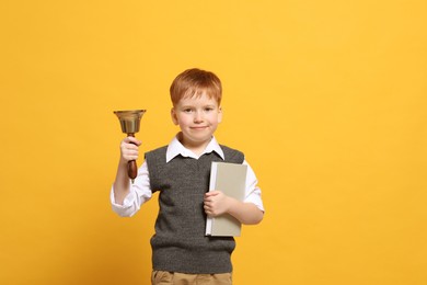 Photo of Pupil with school bell and book on orange background