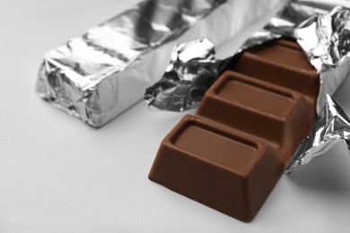 Tasty chocolate bars wrapped in foil on white table, closeup. Space for text