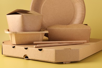 Photo of Eco friendly food packaging. Paper containers and tableware on pale yellow background, closeup