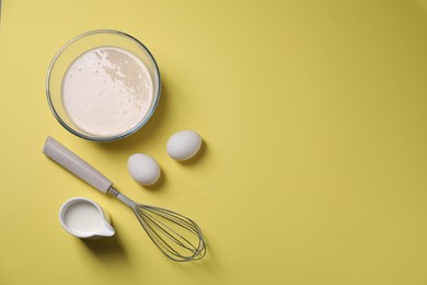Photo of Metal whisk, dough in bowl, eggs and milk on pale yellow background, flat lay. Space for text