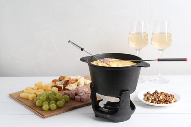 Photo of Fondue pot with tasty melted cheese, forks, wine and different snacks on white wooden table