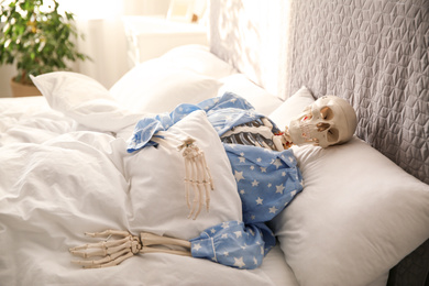 Human skeleton in pajamas lying on bed indoors