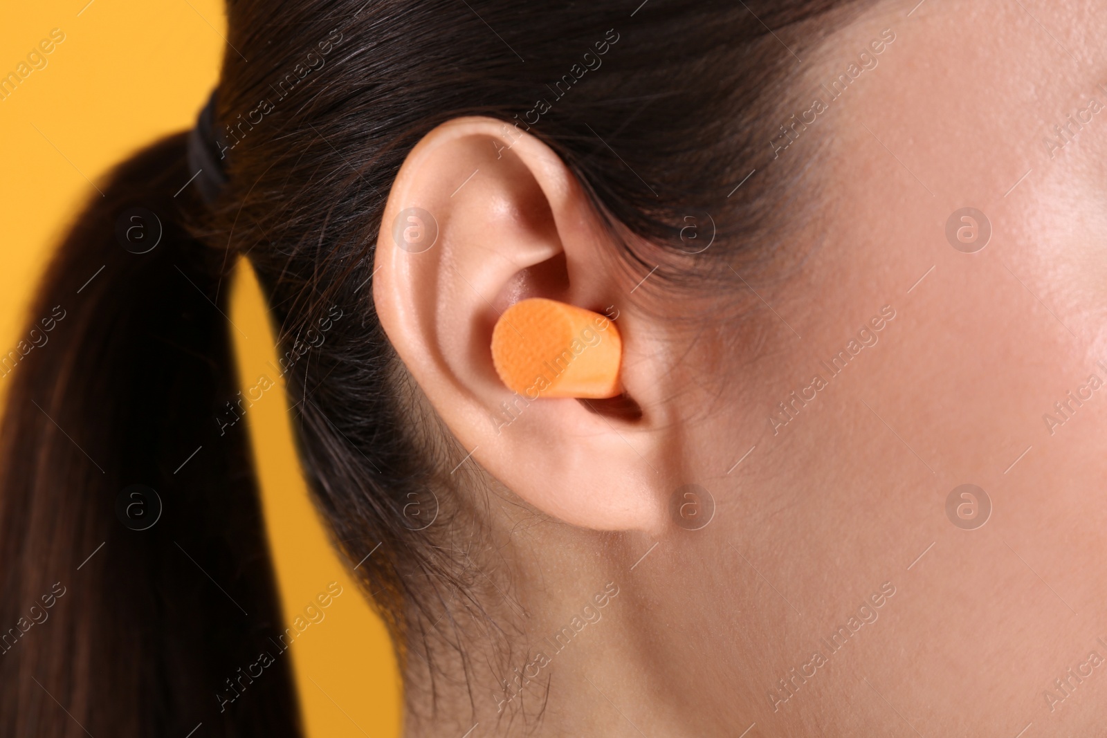 Photo of Young woman wearing foam ear plug on yellow background, closeup