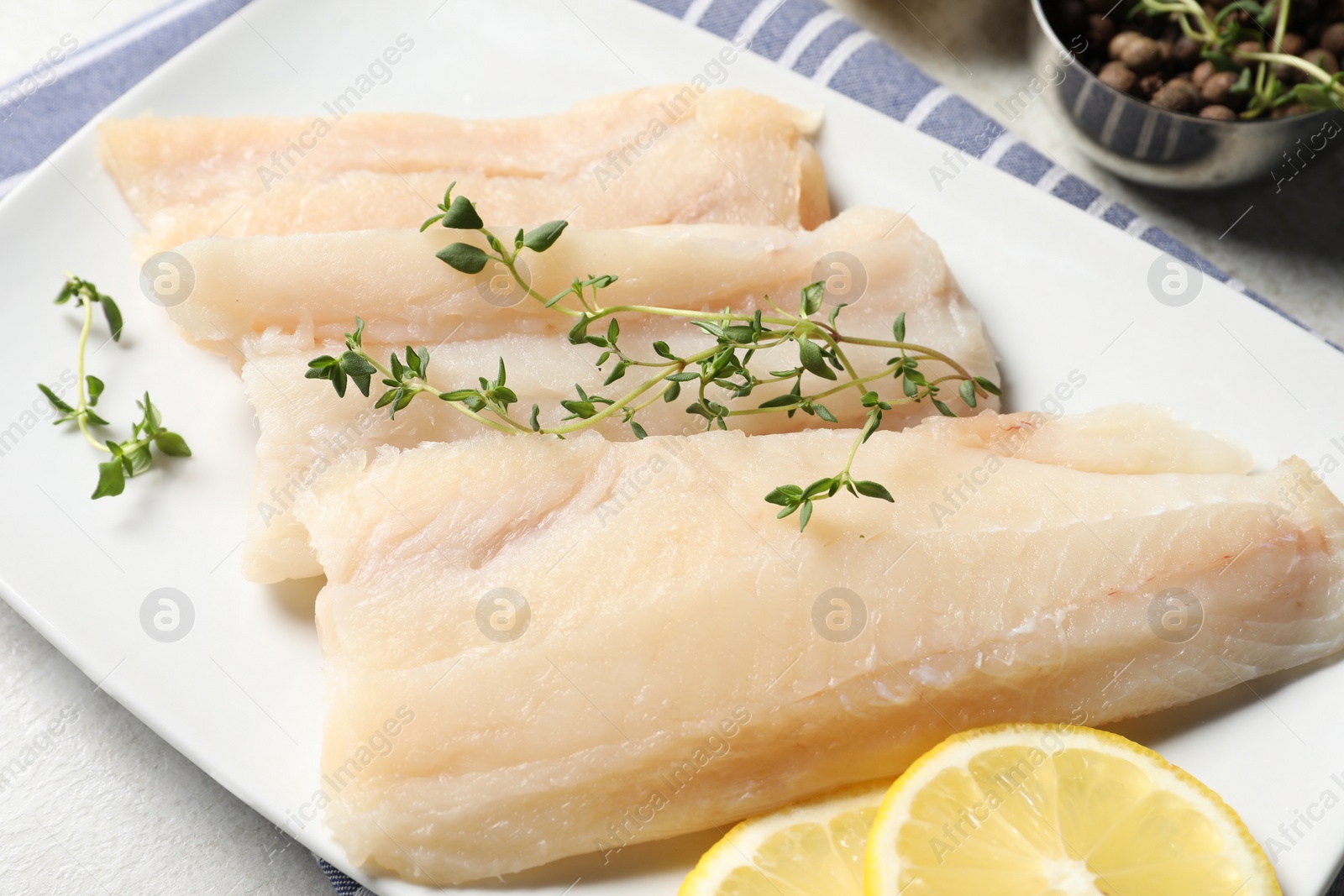 Photo of Pieces of raw cod fish on light grey table, closeup