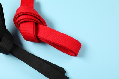 Photo of Red and black karate belts on light blue background, flat lay. Space for text