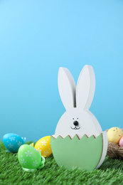 Photo of Easter bunny figure and dyed eggs on green grass against light blue background