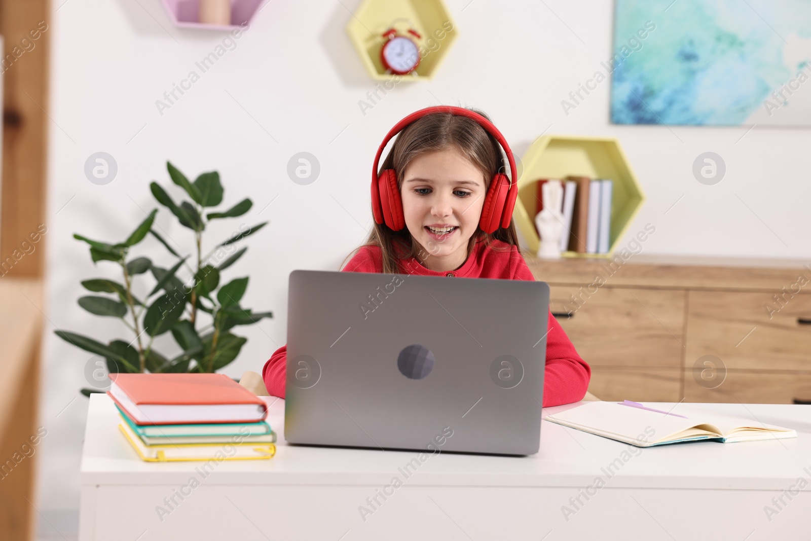 Photo of E-learning. Cute girl using laptop and headphones during online lesson at table indoors