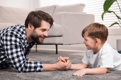 Photo of Arm wrestling. Smiling dad playing with his son at home