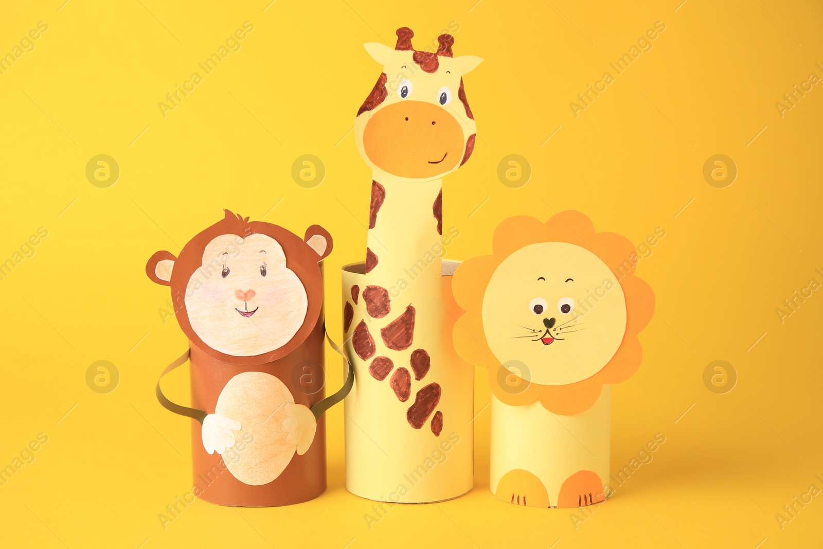 Photo of Toy monkey, giraffe and lion made from toilet paper hubs on yellow background. Children's handmade ideas