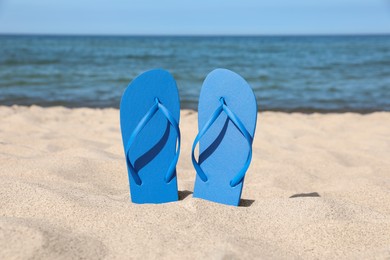 Photo of Stylish blue flip flops on beach sand