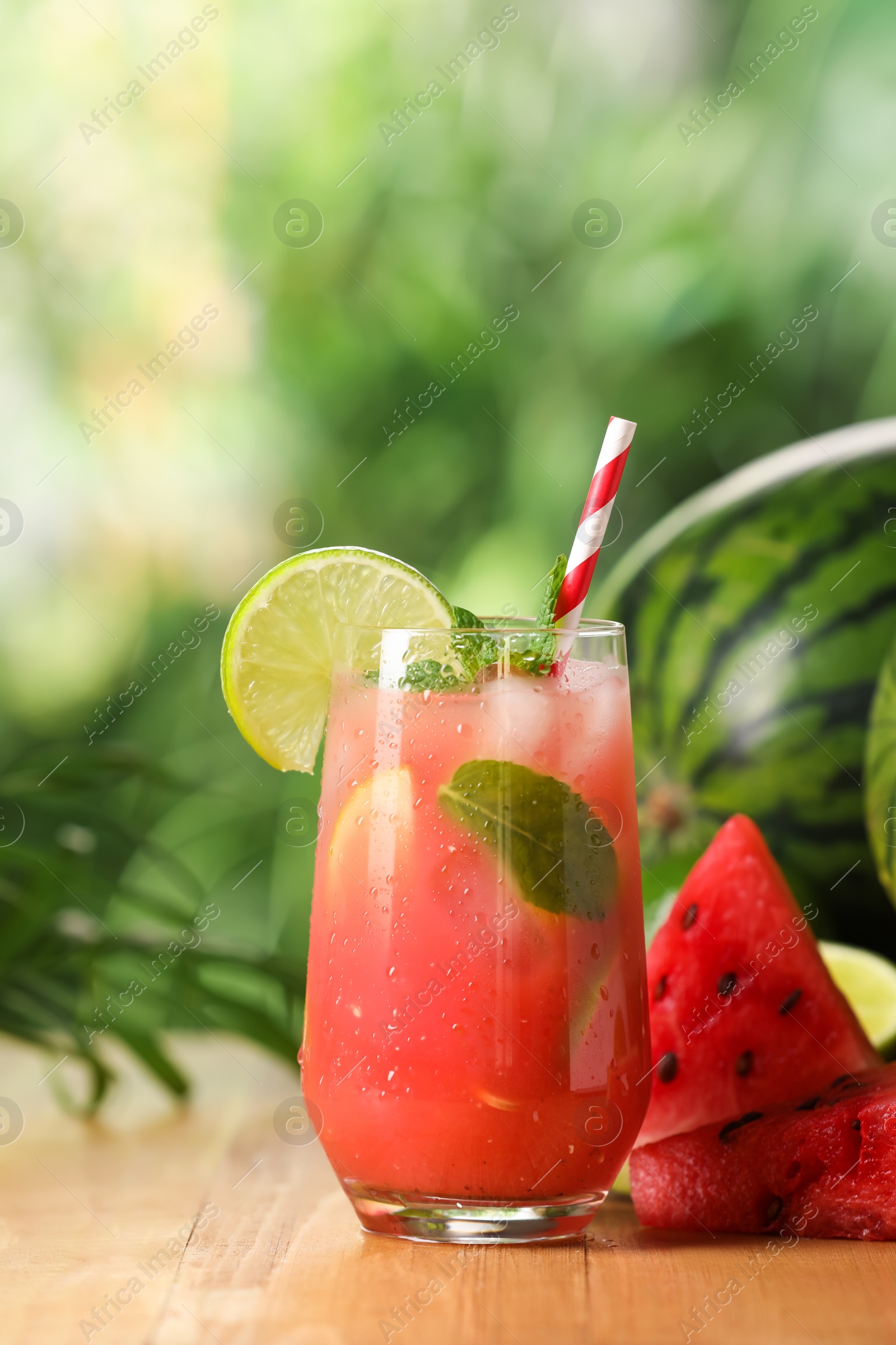 Photo of Glass of freshly made watermelon juice with lime and mint on wooden table outdoors
