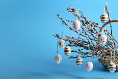 Photo of Wicker basket with beautiful willow branches and painted eggs on light blue background, space for text. Easter decor