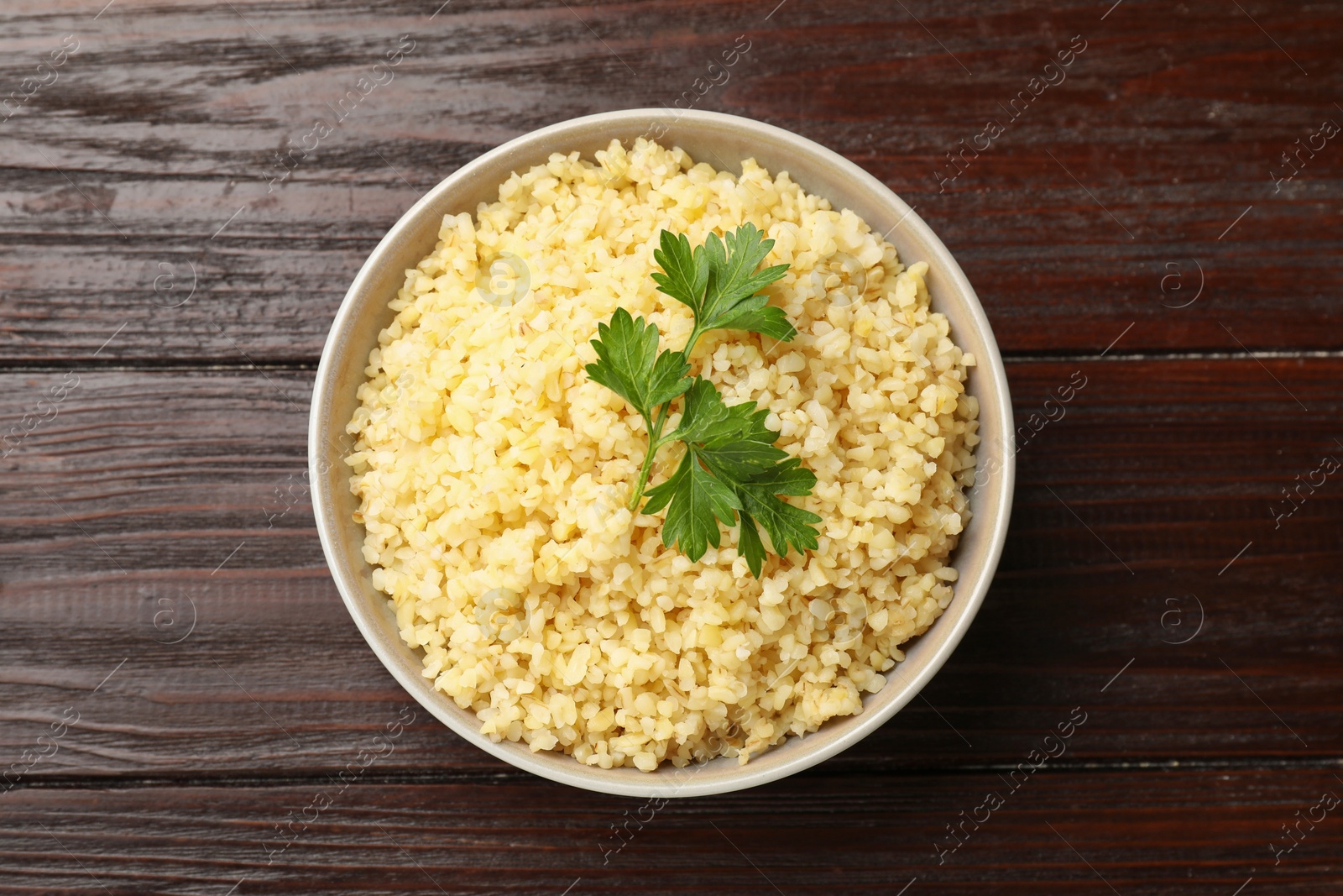 Photo of Delicious bulgur with parsley in bowl on wooden table, top view