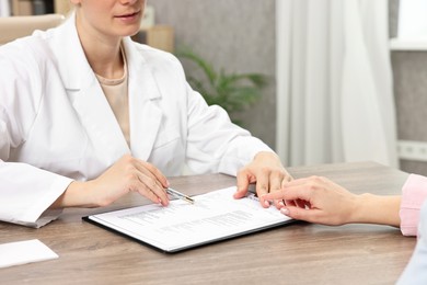 Photo of Doctor with results of pregnancy test consulting patient at wooden table in clinic, closeup