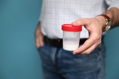 Photo of Donor holding container with sperm on turquoise background, closeup. Space for text