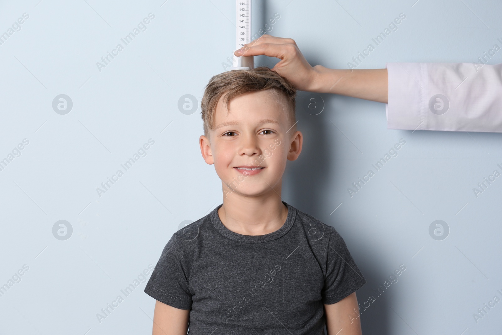 Photo of Doctor measuring little boy's height on light background