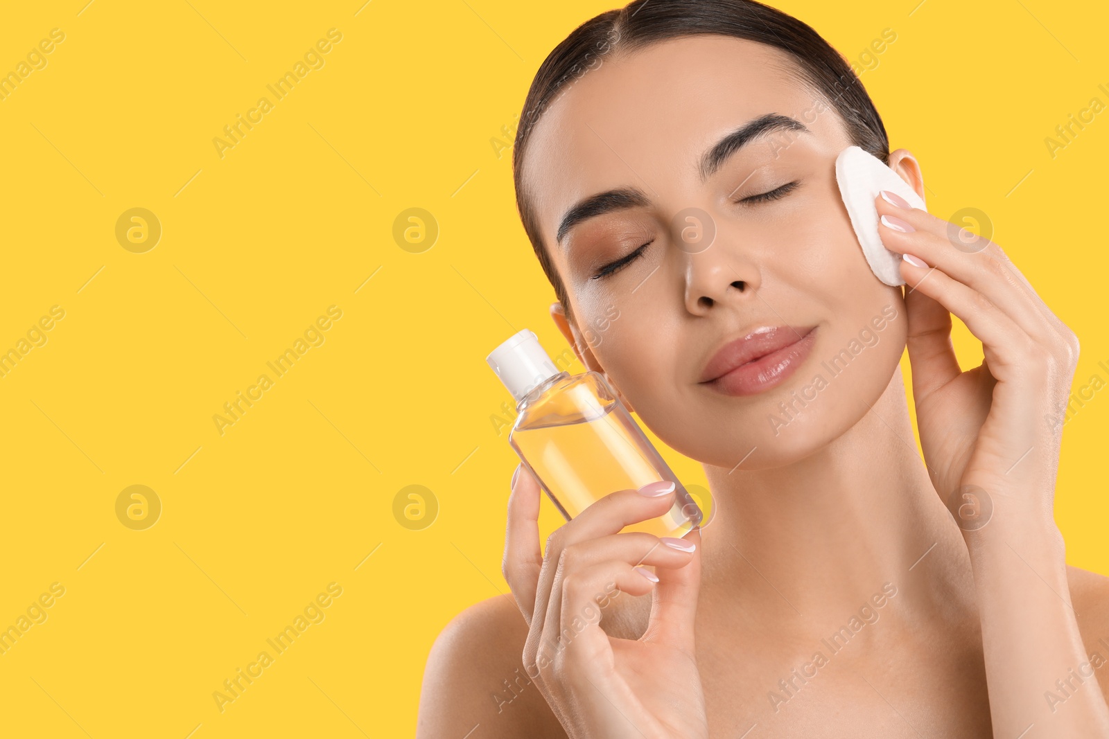 Photo of Beautiful woman removing makeup with cotton pad on yellow background. Space for text