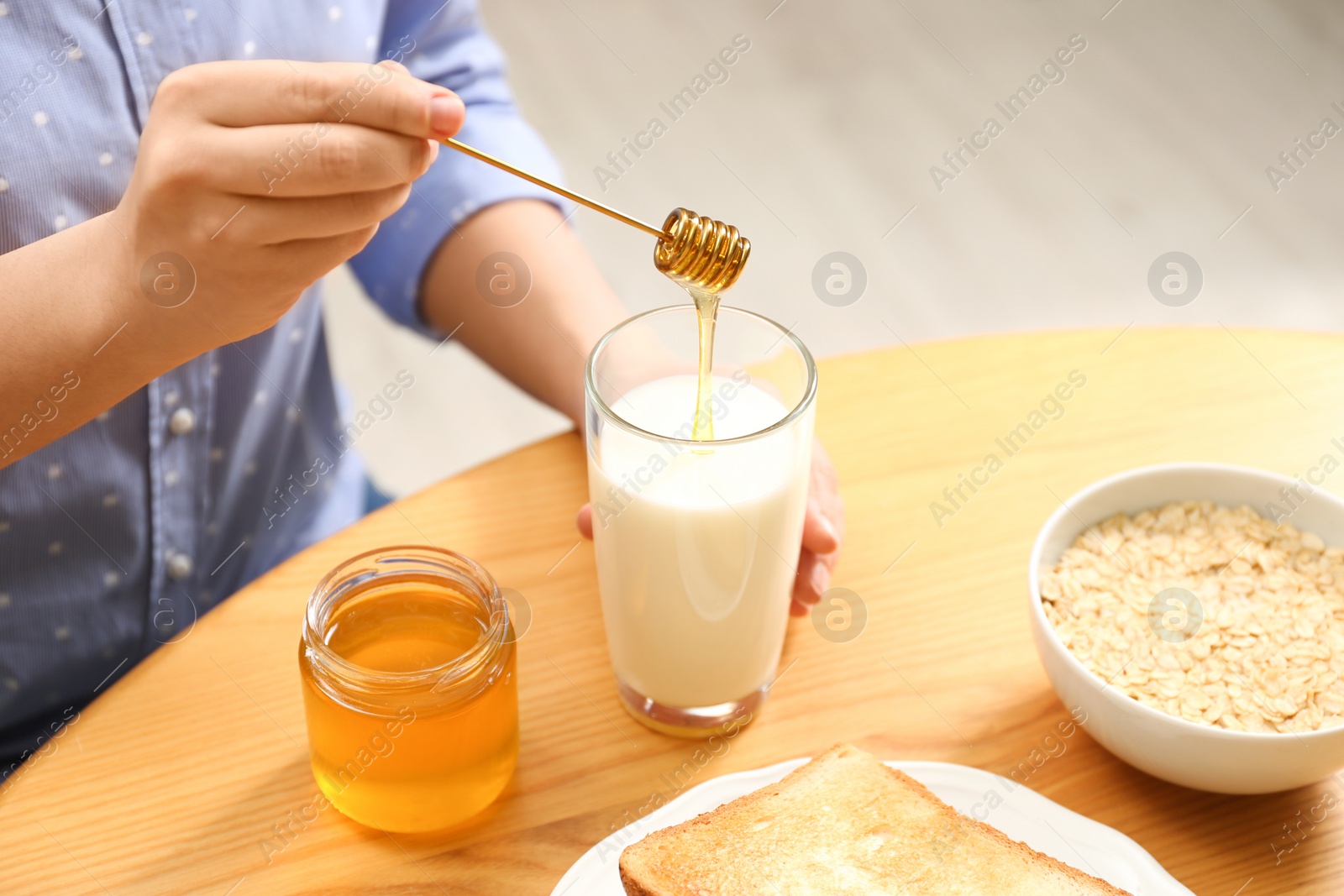 Photo of Woman adding honey to milk at table, closeup