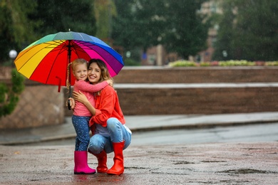 Photo of Happy mother and daughter with bright umbrella under rain outdoors