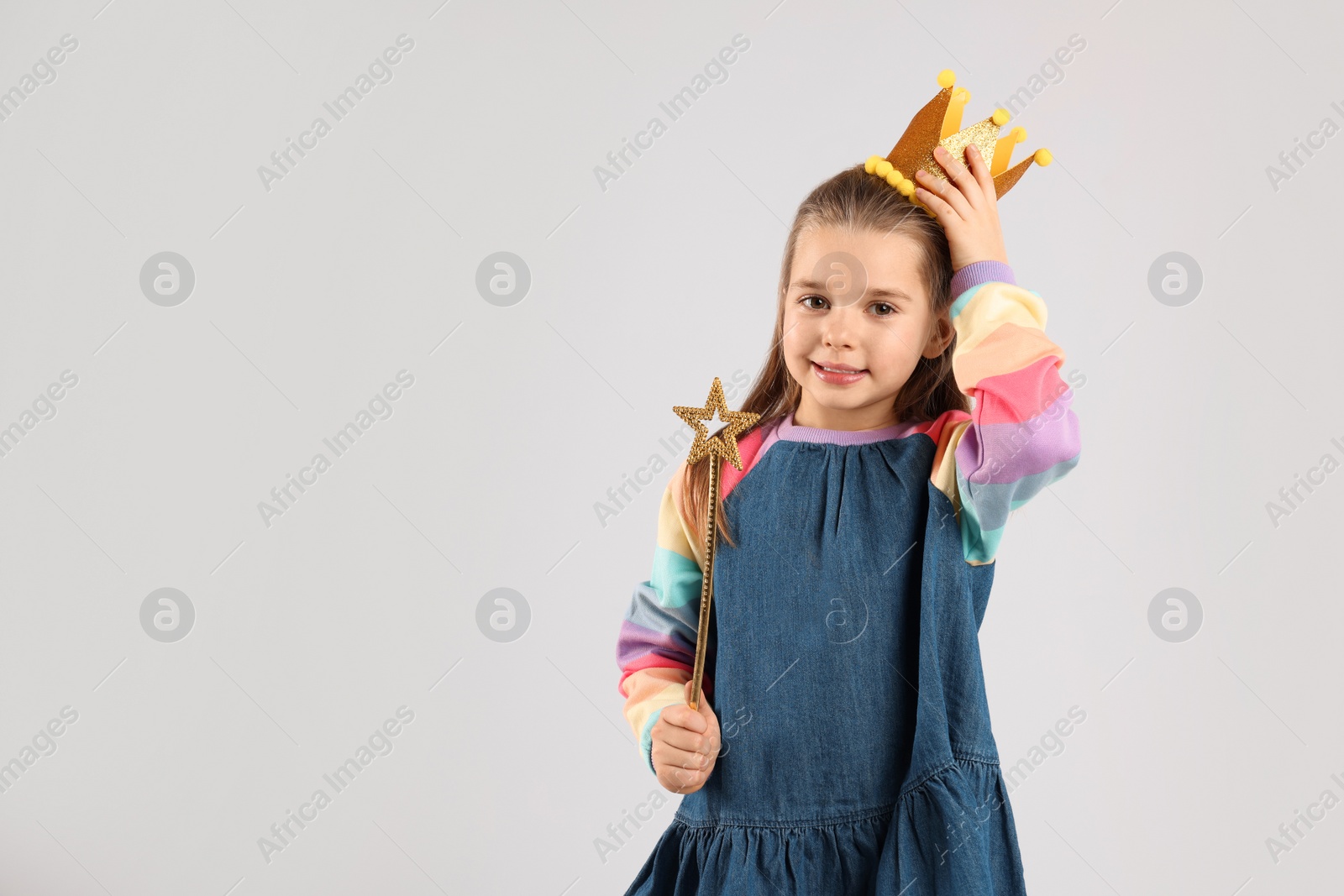 Photo of Cute girl in golden crown with magic wand on light grey background, space for text. Little princess