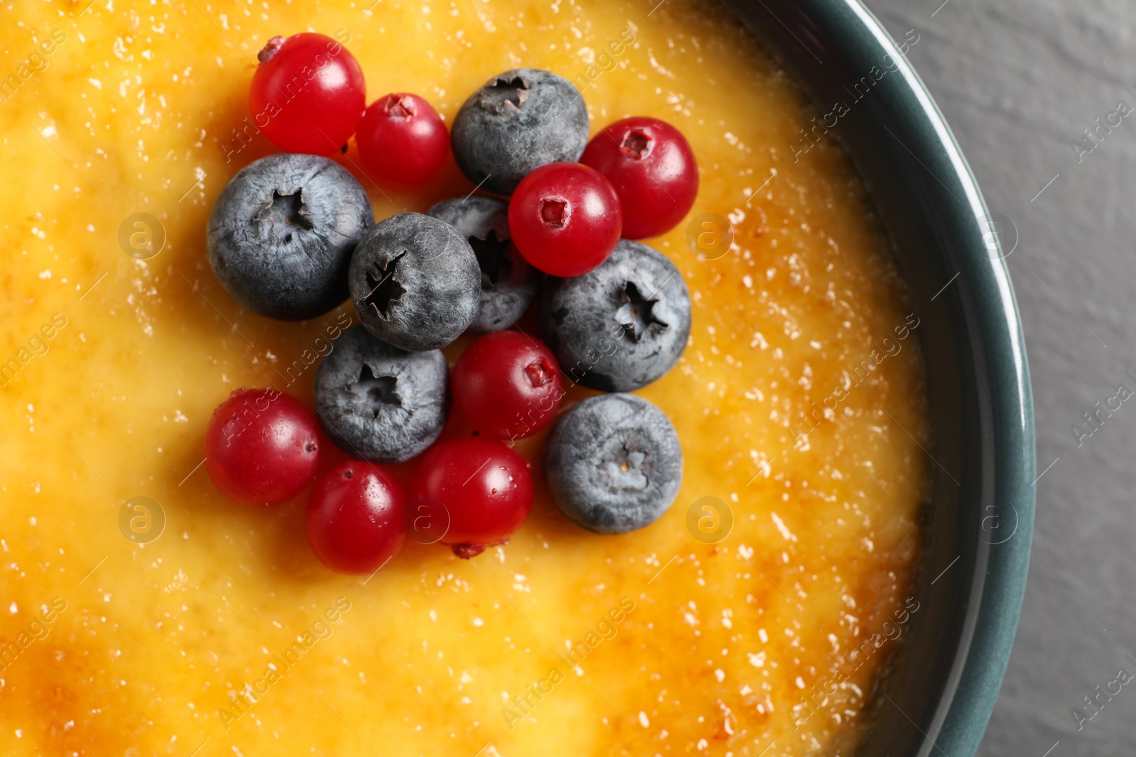 Photo of Delicious creme brulee with fresh berries on black table, closeup