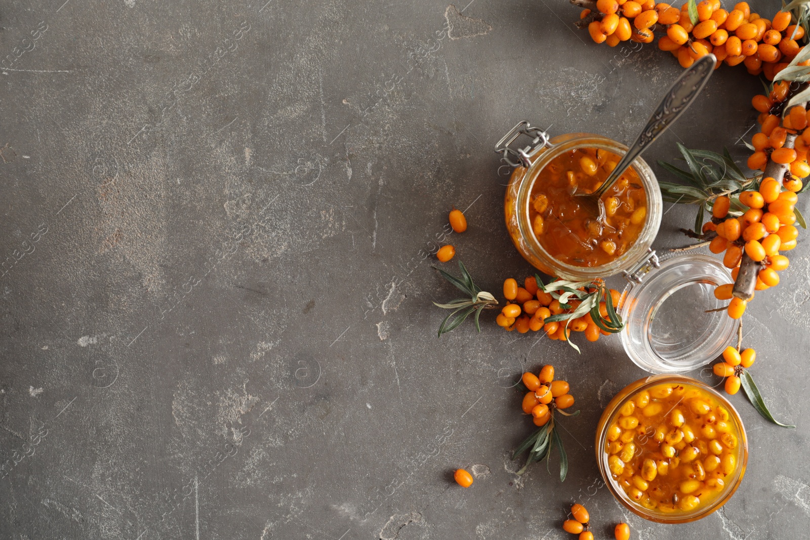 Photo of Delicious sea buckthorn jam and fresh berries on grey table, flat lay. Space for text