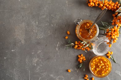 Delicious sea buckthorn jam and fresh berries on grey table, flat lay. Space for text