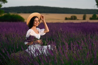 Beautiful young woman with bouquet sitting in lavender field