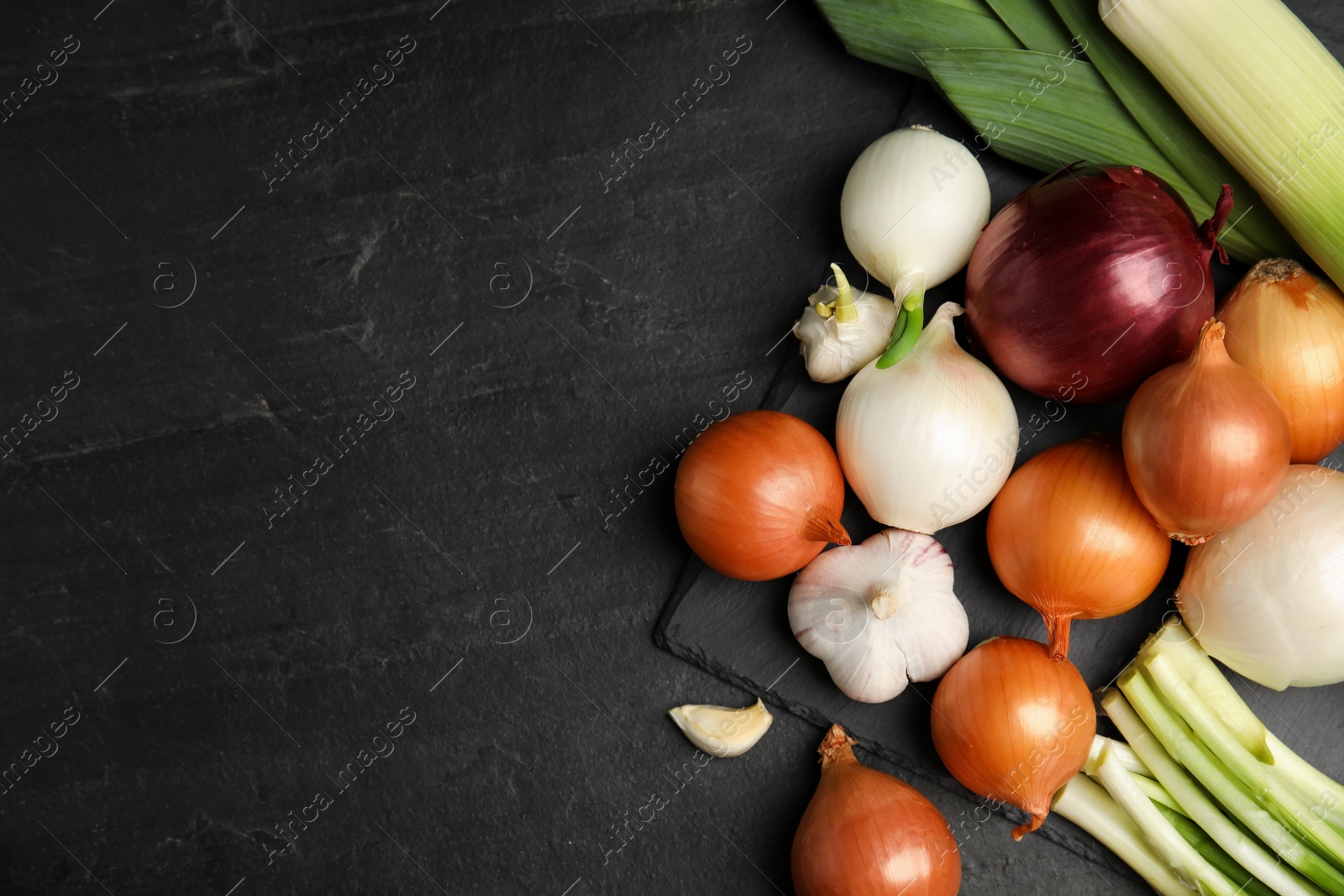 Photo of Fresh onion bulbs, leeks and garlic on black table, flat lay. Space for text