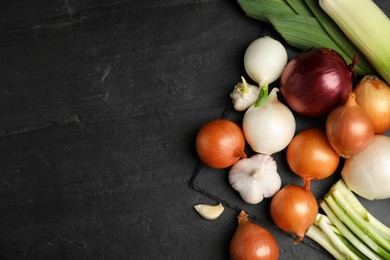 Photo of Fresh onion bulbs, leeks and garlic on black table, flat lay. Space for text