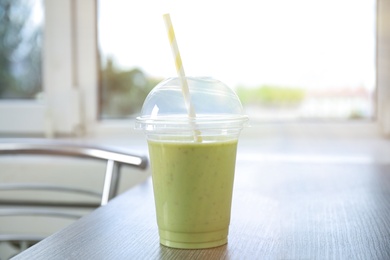 Tasty fresh milk shake in plastic cup on table indoors