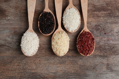 Flat lay composition with brown and other types of rice in spoons on wooden background