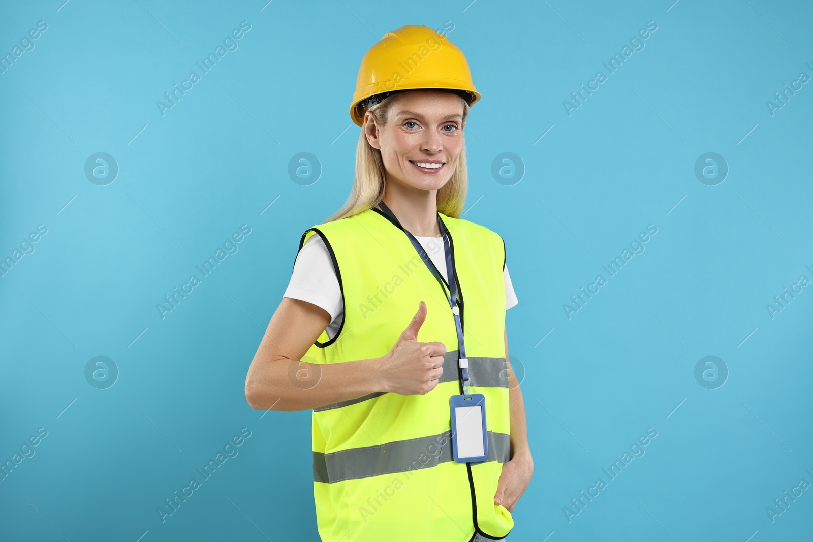 Photo of Engineer with hard hat and badge showing thumb up on light blue background