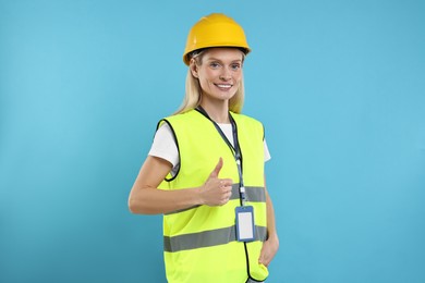 Engineer with hard hat and badge showing thumb up on light blue background