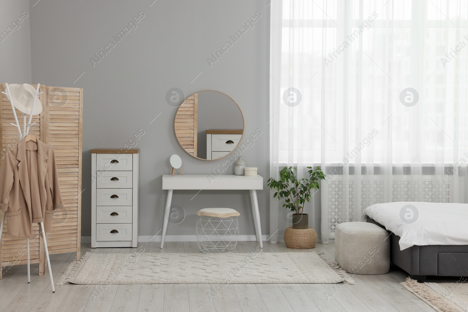 Photo of Stylish bedroom interior with bed, ottoman, dressing table and chest of drawers