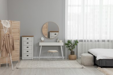 Stylish bedroom interior with bed, ottoman, dressing table and chest of drawers