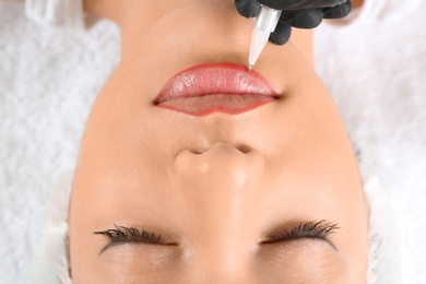 Young woman getting permanent makeup on lips in beautician salon, closeup