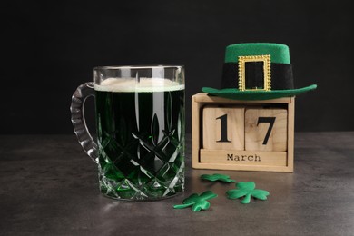 Photo of St. Patrick's day celebrating on March 17. Green beer, wooden block calendar, leprechaun hat and decorative clover leaves on grey table