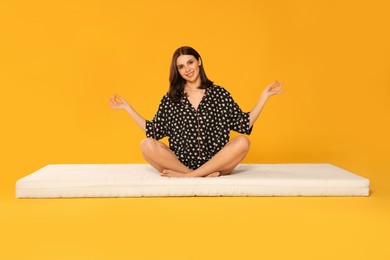Young woman meditating on soft mattress against orange background