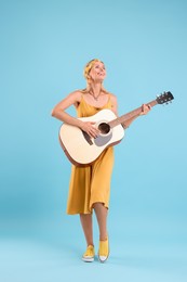 Photo of Happy hippie woman playing guitar on light blue background